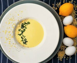 Yellow Avgolemono soup in a bowl next to lemons and eggs