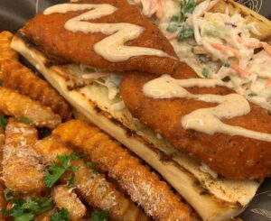 A hoagie topped with slaw, fried rockfish, and a creamy dressing, and served with french fries.