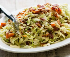 Plate of cabbage topped with pieces of bacon.
