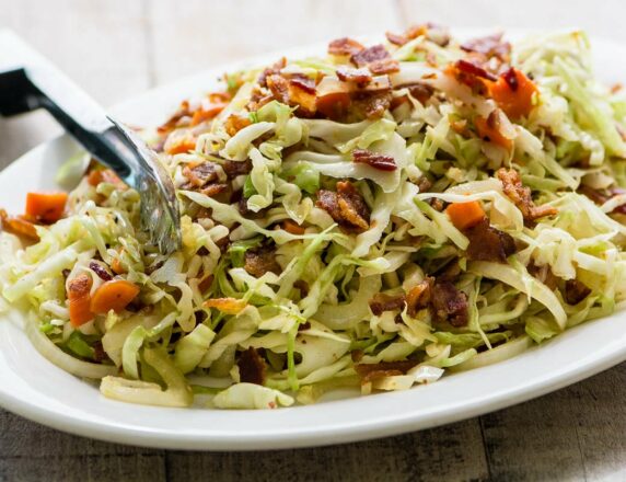 Plate of cabbage topped with pieces of bacon.
